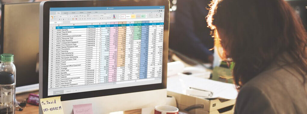 Ein Person sitzt an einem Schreibtisch mit PC. Auf dem Bildschirm werden Excel-Tabellen angezeigt.