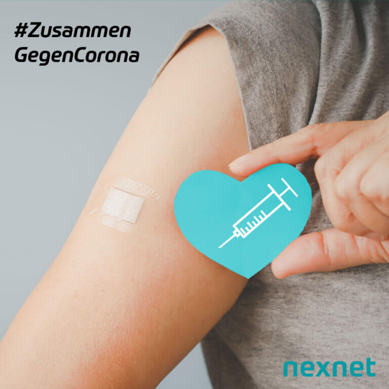 Das Bild zeigt den Arm mit Pflaster einer Person, die sich gerade impfen lies. Außerdem hält die Person in der anderen Hand ein Papierherz auf dem eine Spritze zu sehen ist. Neben dem Arm ist der Schriftzug nexnet: #ZusammenGegenCorona zu lesen.