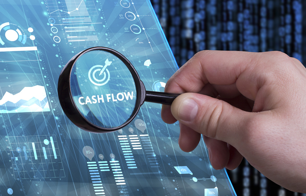 Cashflow Monitoring mit nexnet. Das Bild zeigt ein Hologram, auf dem Cashflow zu lesen ist und das einige Datenströme zeigt. Und es ist eine Hand zu sehen, die eine Lupe über dem Wort Cashflow hält.