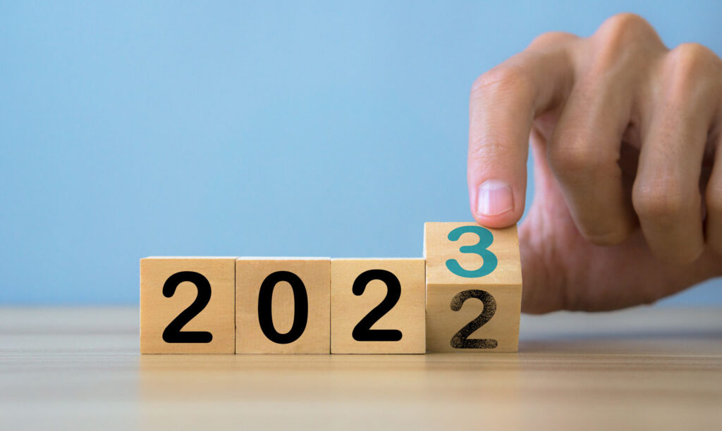 Jahresrückblick 2022 und Ausblick auf 2023. Das Bild zeigt 4 aneinandergereihte Holzwürfel mit der Jahreszahl 2022. Der letzte Würfel wird von einer Hand gedreht, sodass die Zahl 3 erscheint und sich die Jahreszahl 2023 ergibt.