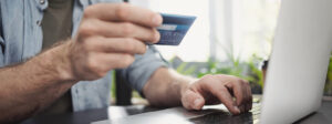 A man sits at his PC and holds his credit card in his hand.