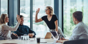 Review of the year with nexnet. The picture shows a group of people in an office. They are in a good mood. One woman is high-fiving another woman. The other people are sitting next to them and smiling.