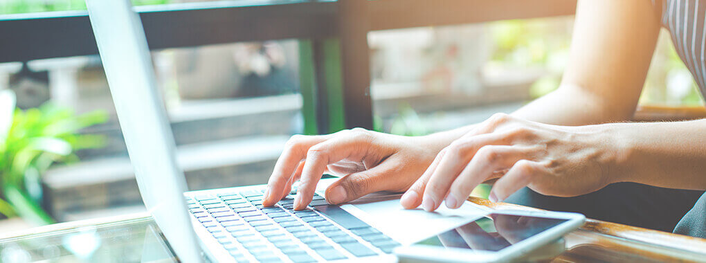 In einer Nahaufnahme sind ein Laptop und ein Handy abgebildet, an denen eine Person arbeitet.