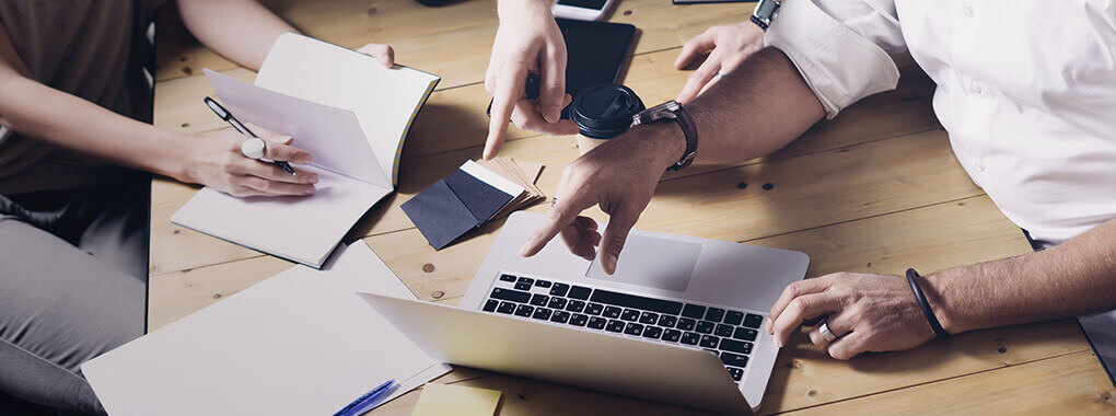Mehrere Personen sitzen an einem Schreibtisch und zeigen auf einen Bildschirm.