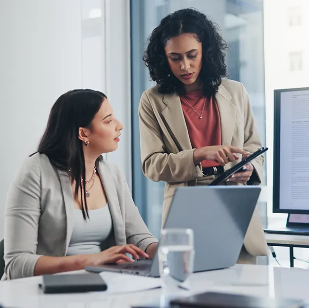 Zwei Geschäftsfrauen analysieren gemeinsam Abrechnungsdetails auf Laptop und Tablet – symbolisch für One-Time Billing und nutzerspezifische Einzelabrechnungen im Finanzkontext.