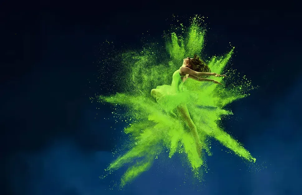 Tänzerin im grünen Kleid springt dynamisch durch eine Explosion aus grünem Farbpulver