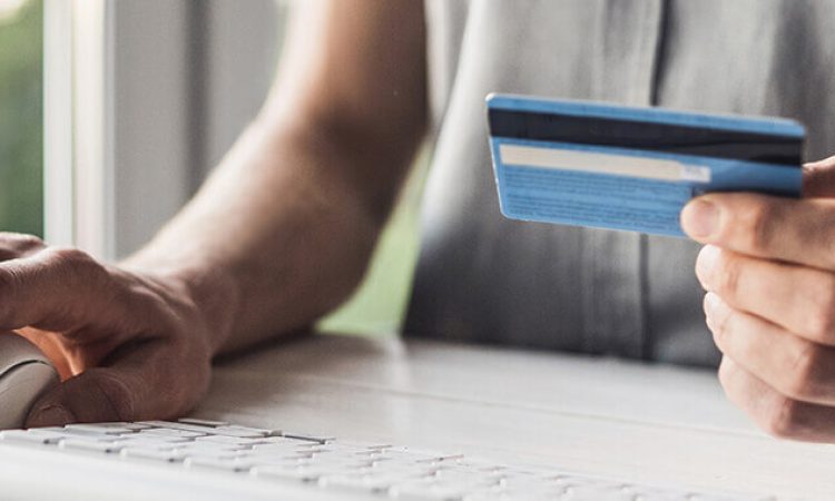 A man sits at his PC and enters his credit card details, which he removes from the card.