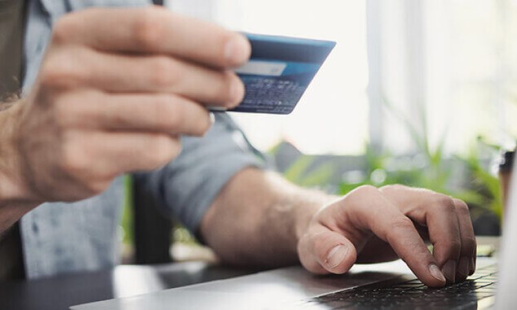 A man sits at his PC and holds his credit card in his hand.