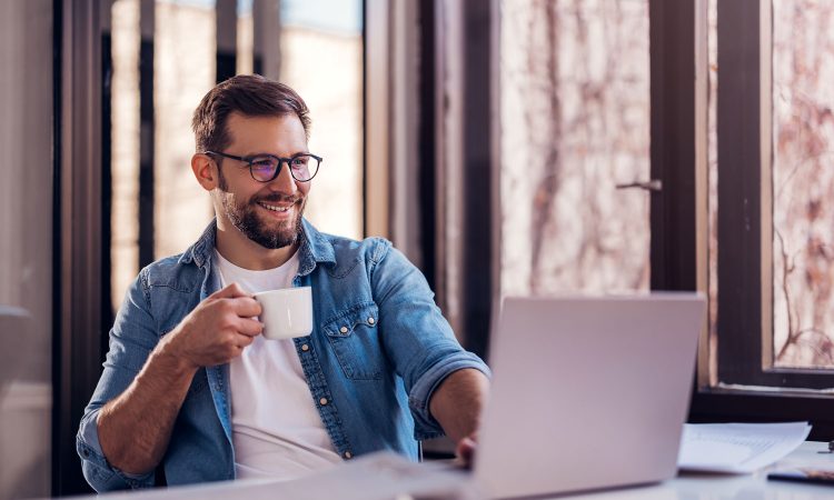 Managing subscriptions with the nexnet solution for subscription billing. The picture shows a satisfied man sitting at a desk. He is holding a coffee cup in his hand and looking at his laptop. He is smiling contentedly.