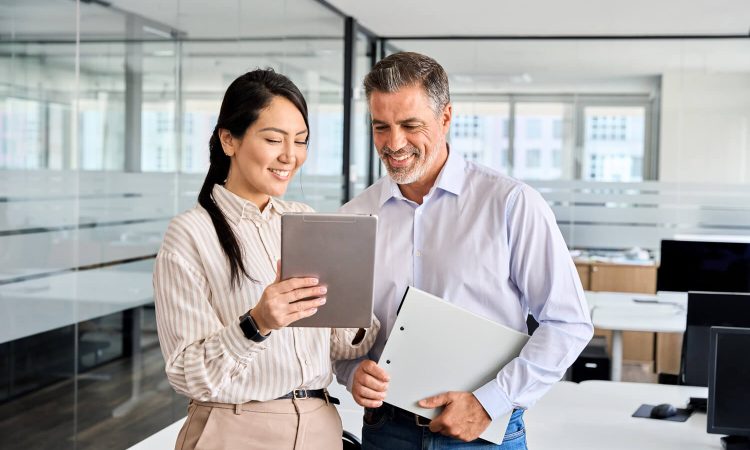 Automated billing with nexnet. The picture shows two people in an office looking at something together on a tablet. The woman is holding the tablet, the man is holding a folder.