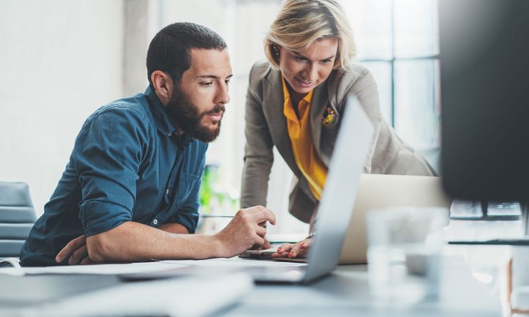 The picture shows a man and a woman working in an office and evaluating the information displayed on the computer screen together.