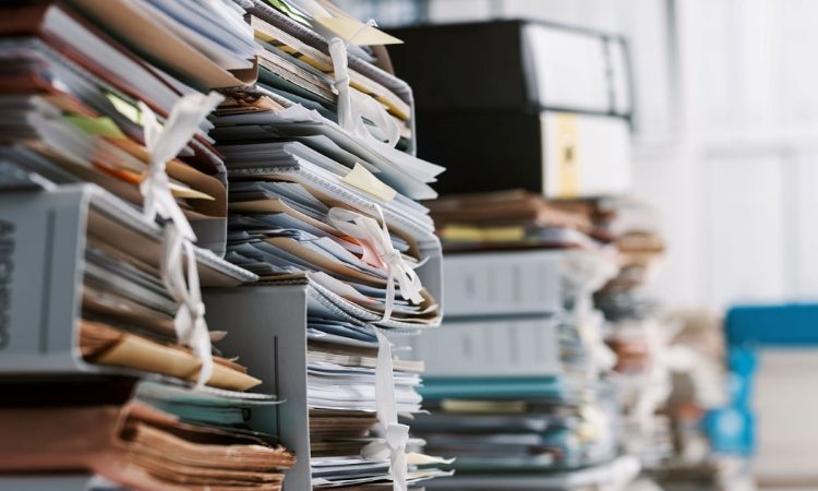 Das Bürokratieentlastungsgesetz IV ist da. Das Bild zeigt eine Nahaufnahme von diversen Papieren und Ordnern, aufgestapelt auf Tischen in einem Büro.