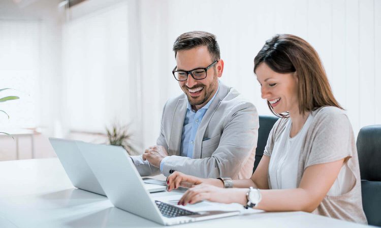 A man and a woman work happily on their laptops in a modern office.