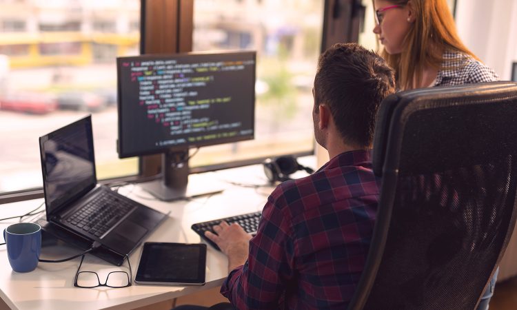 The picture shows 2 people in an office at a desk. Coding can be seen on the computer screen. IT plays an important role for nexnet.