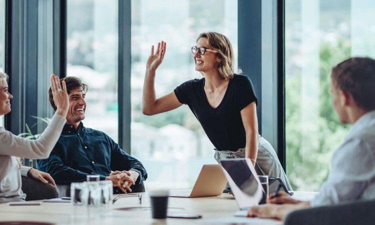 Review of the year with nexnet. The picture shows a group of people in an office. They are in a good mood. One woman is high-fiving another woman. The other people are sitting next to them and smiling.