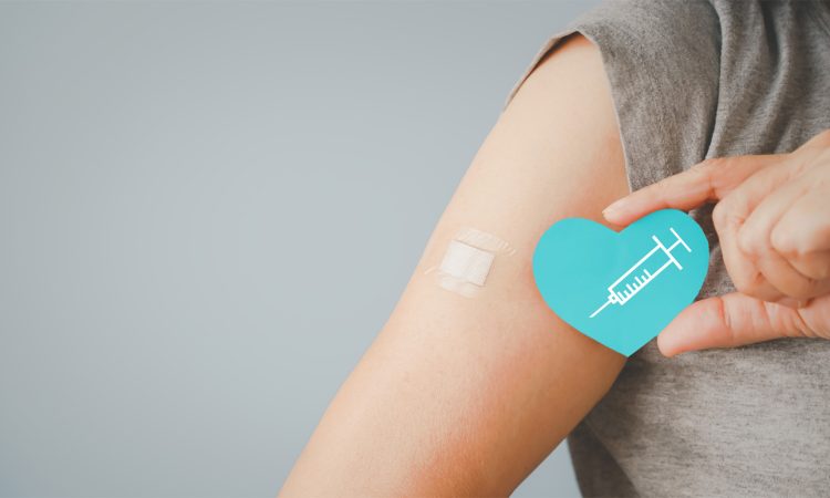 The picture shows the arm with a plaster of a person who has just been vaccinated. The person is also holding a paper heart with a syringe in the other hand. Next to the arm is the lettering nexnet: #TogetherAgainstCorona.