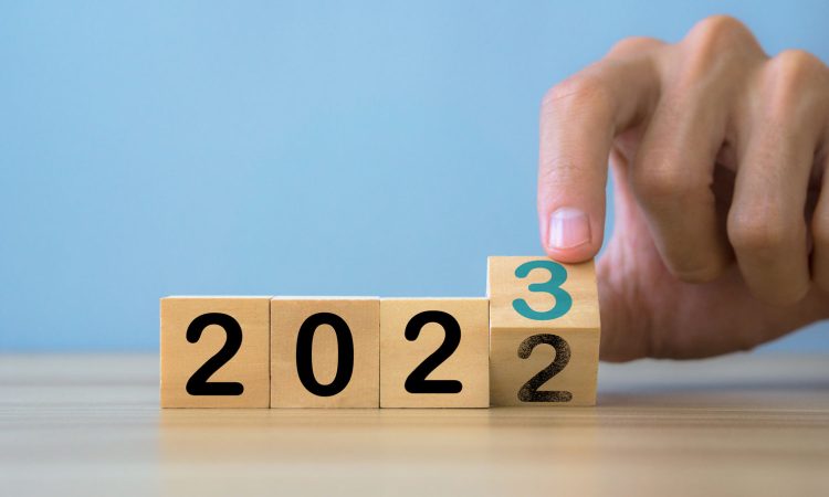 Review of 2022 and outlook for 2023. The picture shows 4 wooden cubes lined up in a row with the year 2022. The last cube is turned by a hand so that the number 3 appears and the year 2023 results.