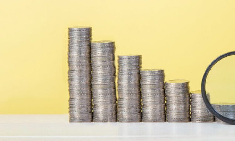 Stacks of coins are arranged in a row in steps. The largest on the left and the smallest on the right. A magnifying glass is pointed at the last, smallest stack of coins.
