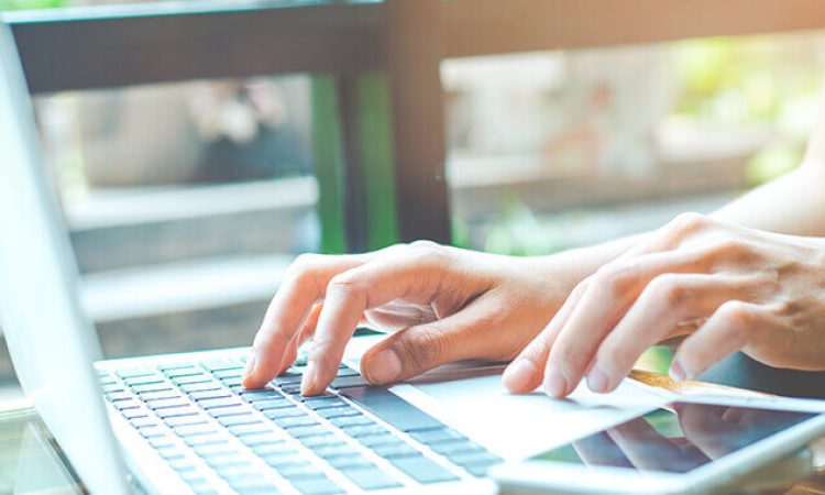 In einer Nahaufnahme sind ein Laptop und ein Handy abgebildet, an denen eine Person arbeitet.