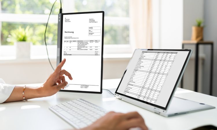 The picture shows a person in an office, working at a desk and looking at two monitors. The monitors show tables and invoices. The person is making a payment reconciliation. Automatic payment reconciliation can be carried out with nexnet.